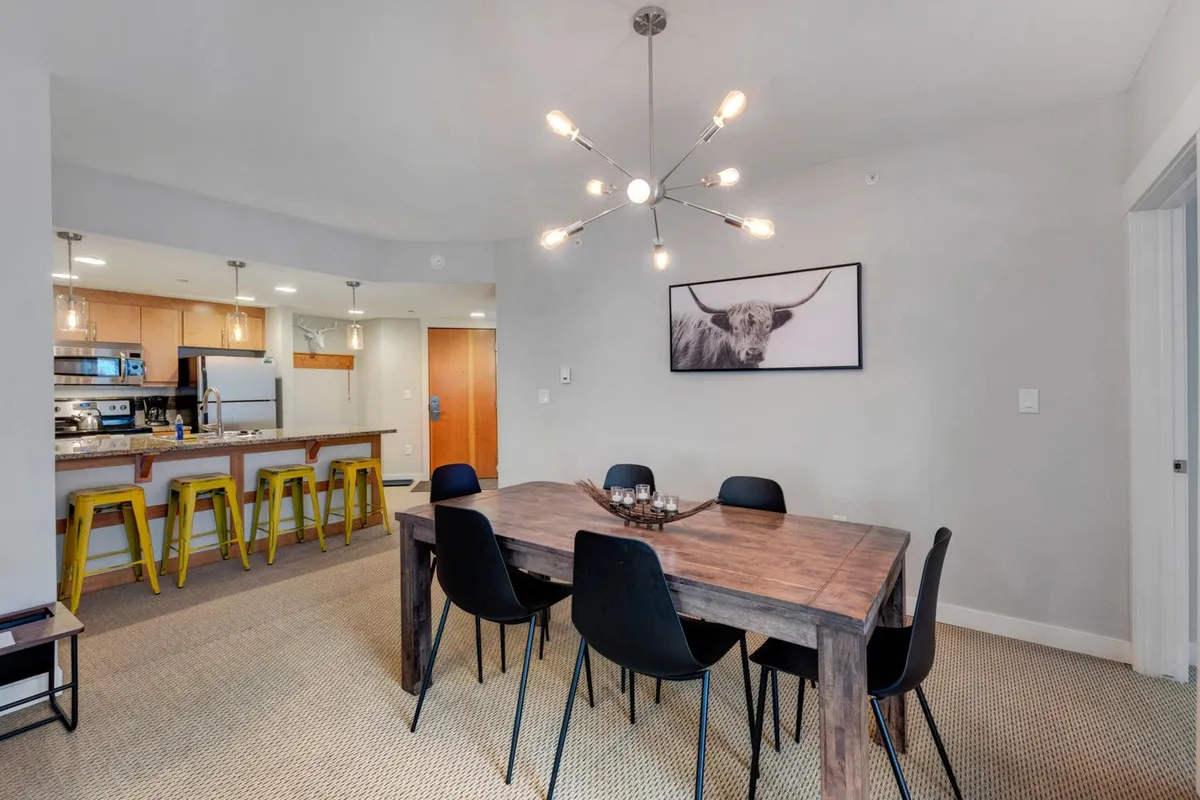 A stylish dining area featuring a large dining table beneath an elegant chandelier. Artwork on the wall adds sophistication, and the setup encourages family dinners, group gatherings, and memorable conversations.