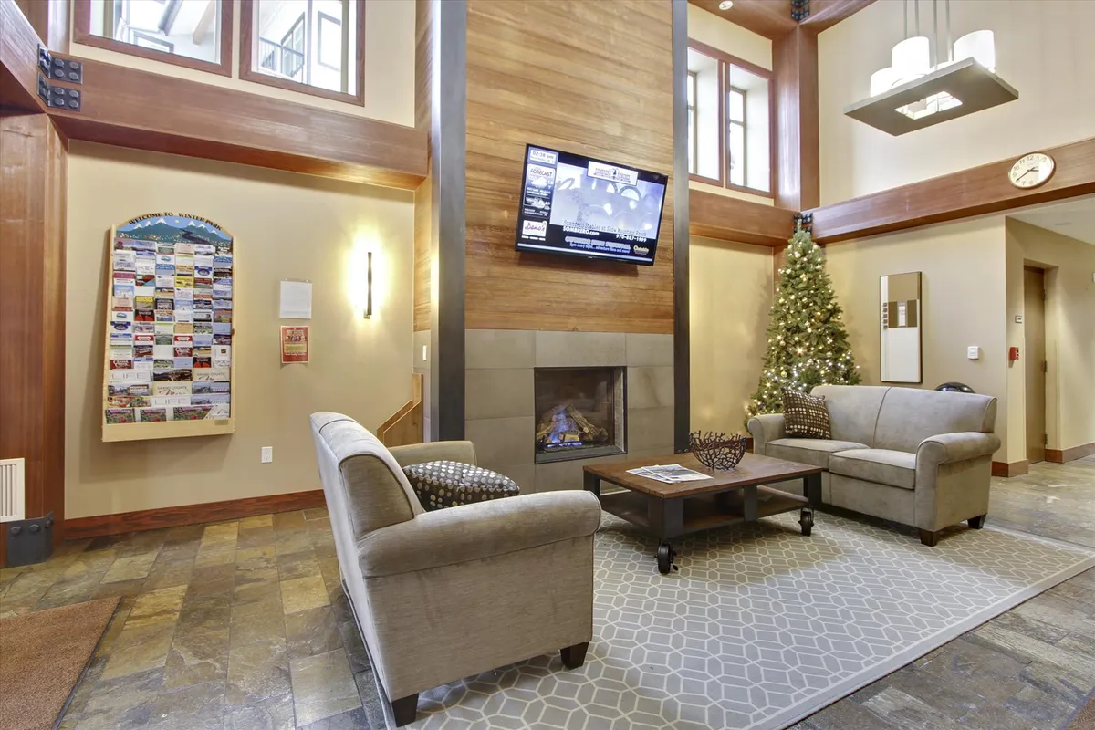 A warm and inviting lobby interior, anchored by a glowing fireplace. Plush seating and festive decorations create a welcoming atmosphere for guests gathering, relaxing, or preparing for their next Winter Park adventure.