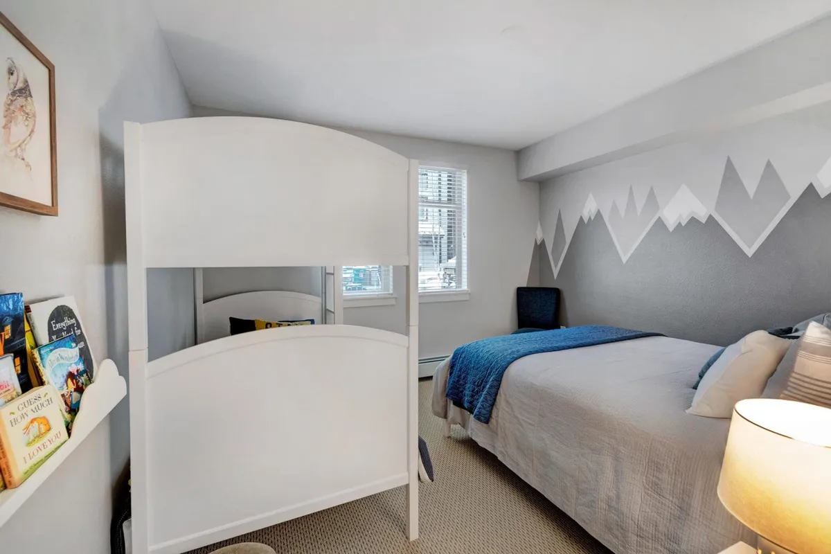 A playful, welcoming kids’ bunk bed setup stands out, framed by a mountain mural, soft lighting, and colorful books. The mood is cheerful and snug, evoking family togetherness and in-condo fun for younger guests.