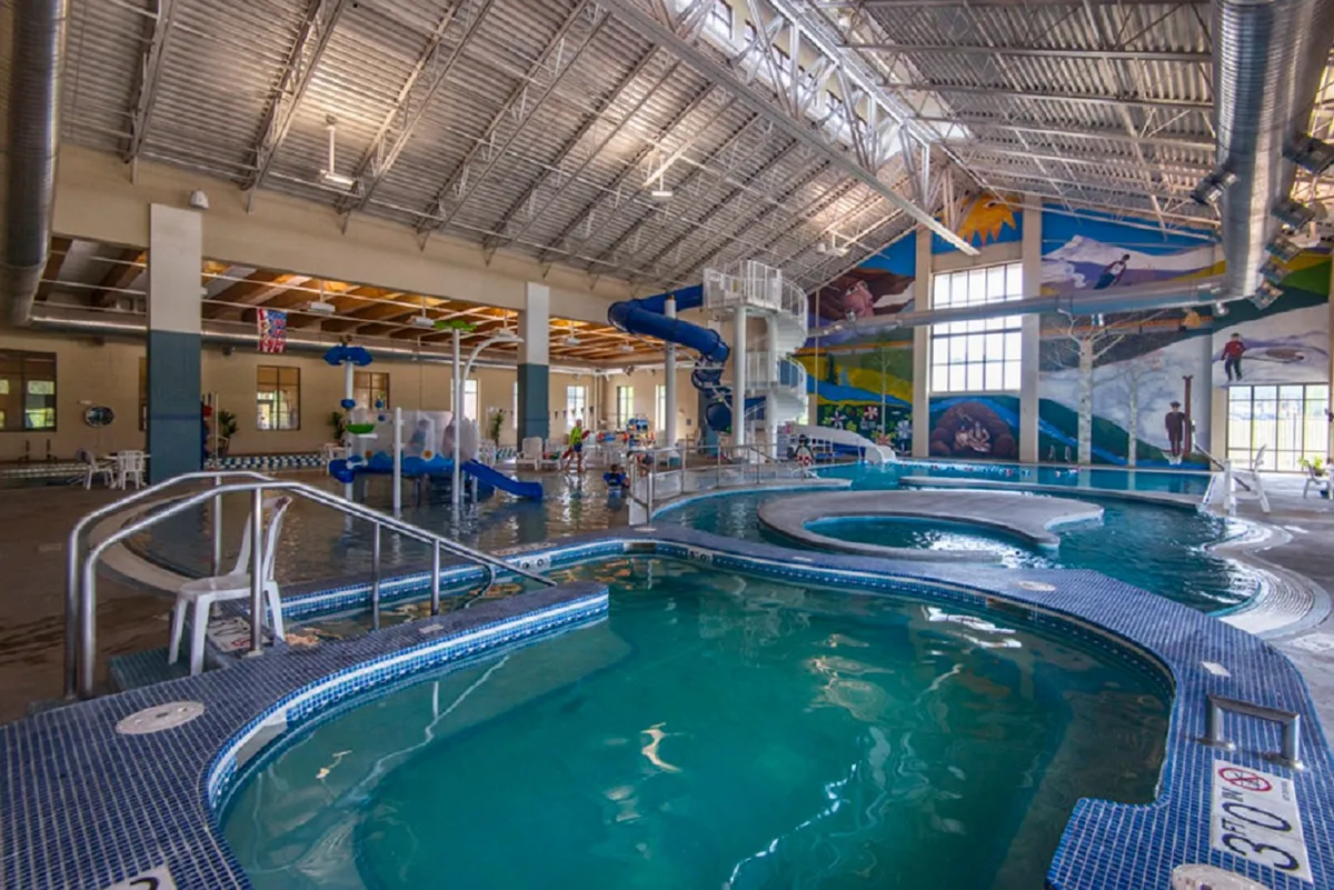 An energetic indoor aquatic center bustling with children playing on colorful water slides and families swimming in the pool. Vibrant murals and bright lighting add a sense of playfulness and fun, making it a lively hub for family recreation and memorable summer moments.