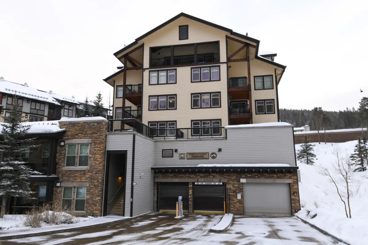 A striking multi-story building with a stone facade stands amidst a snow-blanketed landscape, exuding warmth and coziness. The setting suggests direct proximity to the slopes, with easy winter sports access and après-ski comfort.