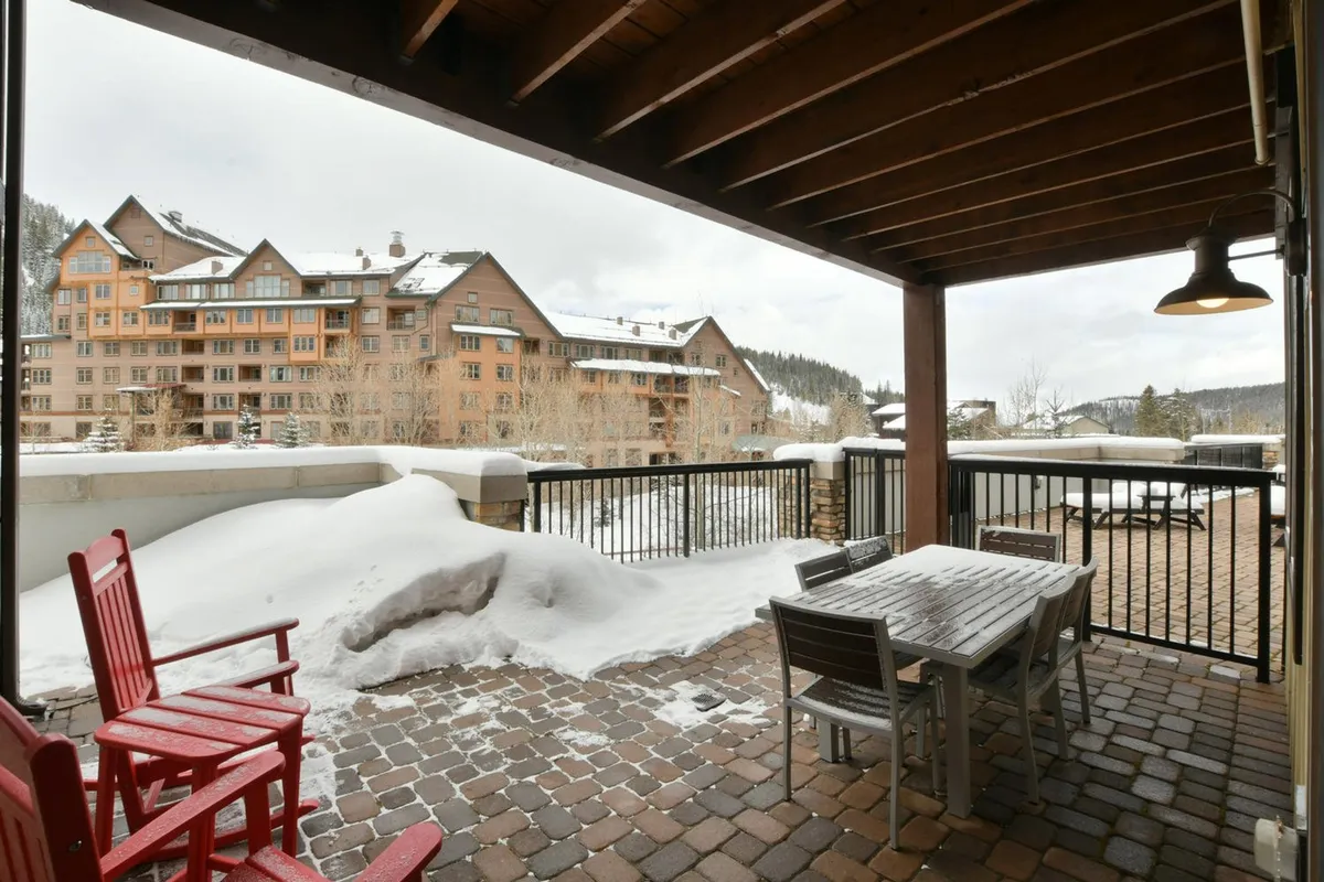 A snowy patio scene with bright red rocking chairs and an outdoor dining set, overlooking a pristine winter landscape. The setup invites guests to savor hot drinks, enjoy casual meals, and watch the snowfall from a cozy outdoor vantage point.