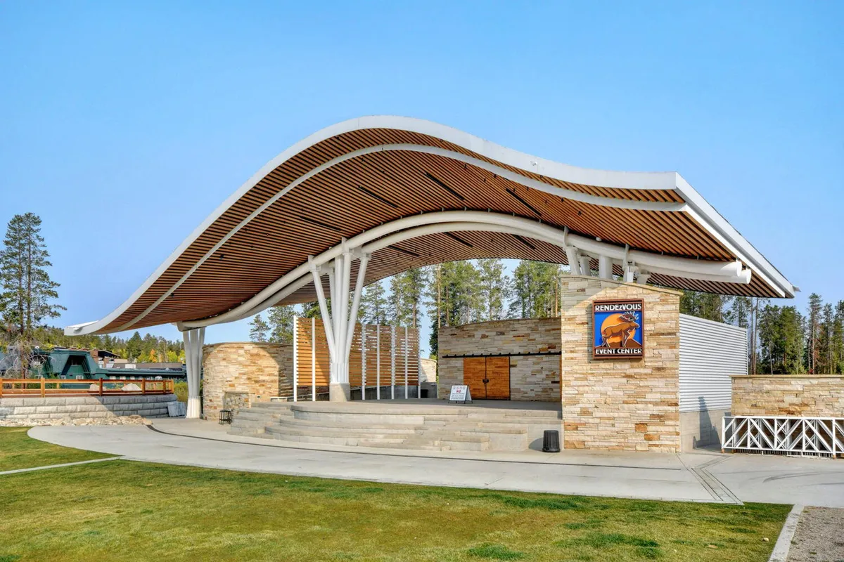 This image shows a modern outdoor stage with a curved roof structure, stone walls, and festival signage. The space is clearly designed for group gatherings, performances, and community celebrations, evoking the spirit of concerts and festivals at Hideaway Park.
