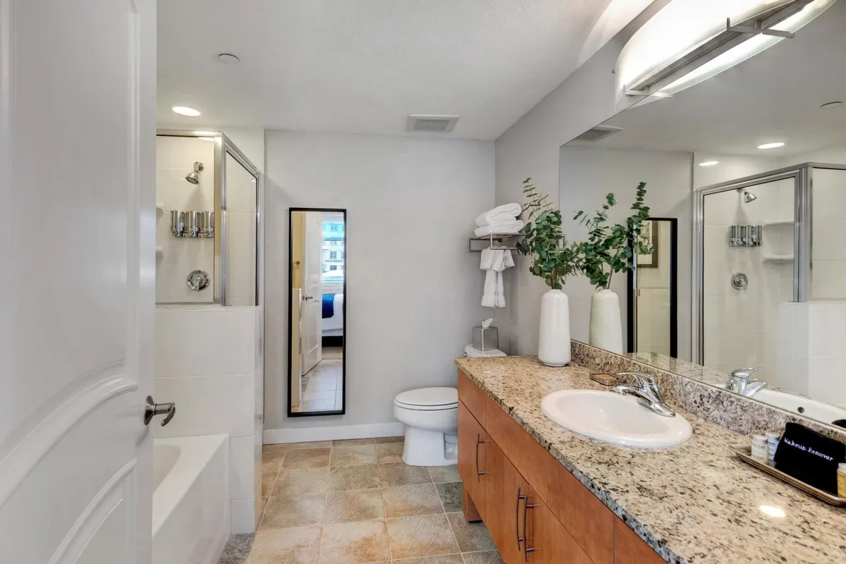 An inviting spa-inspired bathroom featuring a vanity with a large mirror, a sleek sink, a modern tub, a glass-enclosed shower, and a decorative plant. The clean lines and serene décor convey a luxurious and refreshing atmosphere.