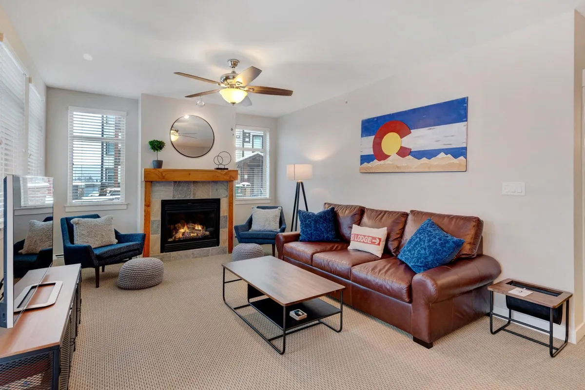 A cozy living room scene featuring a warm fireplace as the focal point, an inviting sofa, and thoughtfully placed artwork on the wall. The space is softly lit, with plush seating arranged to encourage conversation and relaxation, perfect for unwinding after a day of mountain adventures.