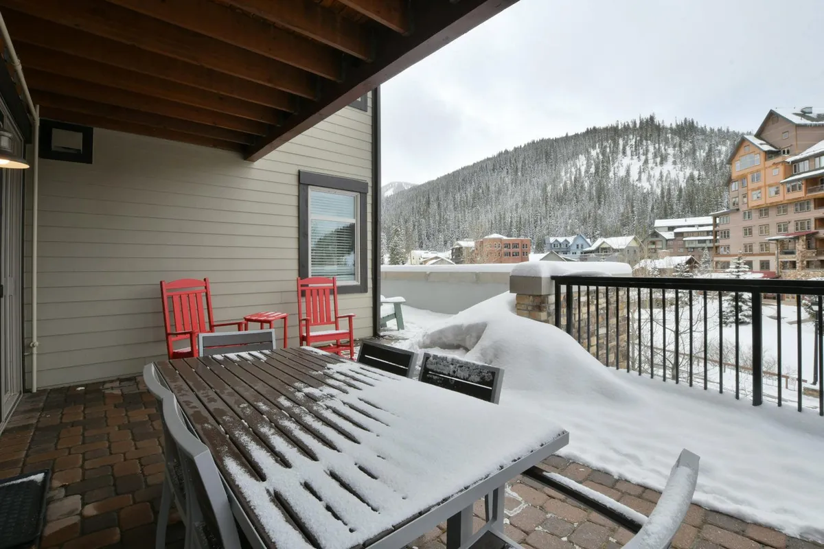 A private covered deck with a snow-covered table and red chairs, overlooking a tranquil mountain vista. The outdoor setting feels peaceful and inviting, perfectly suited for sipping coffee or gathering with friends while taking in the breathtaking scenery.